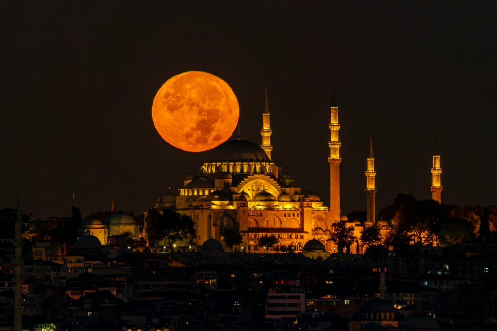A stunning view of the illuminated Suleymaniye Mosque with a full moon rising behind, capturing the essence of Istanbul