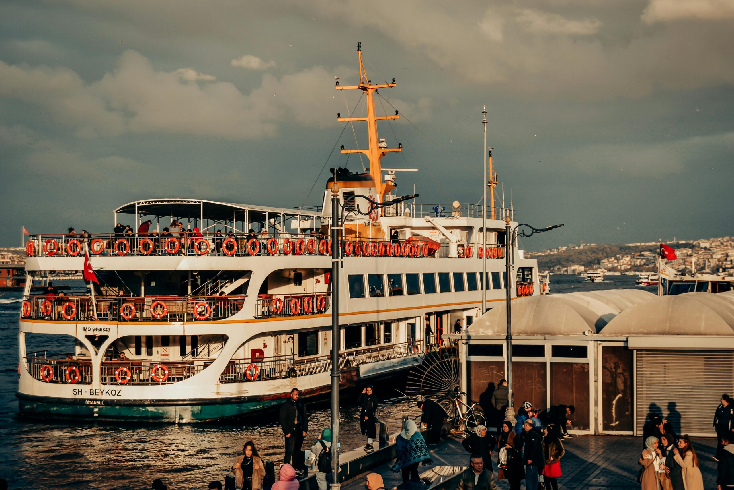 Home A vibrant harbor with a ferry docked, bustling with people, captured during sunset.