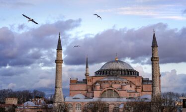 Stunning view of the Hagia Sophia under a dramatic sky with birds flying in Istanbul, Turkey.