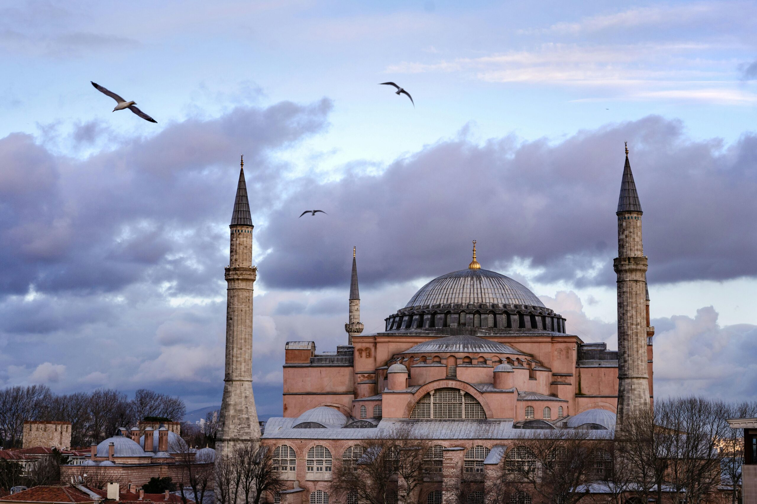 Stunning view of the Hagia Sophia under a dramatic sky with birds flying in Istanbul, Turkey.