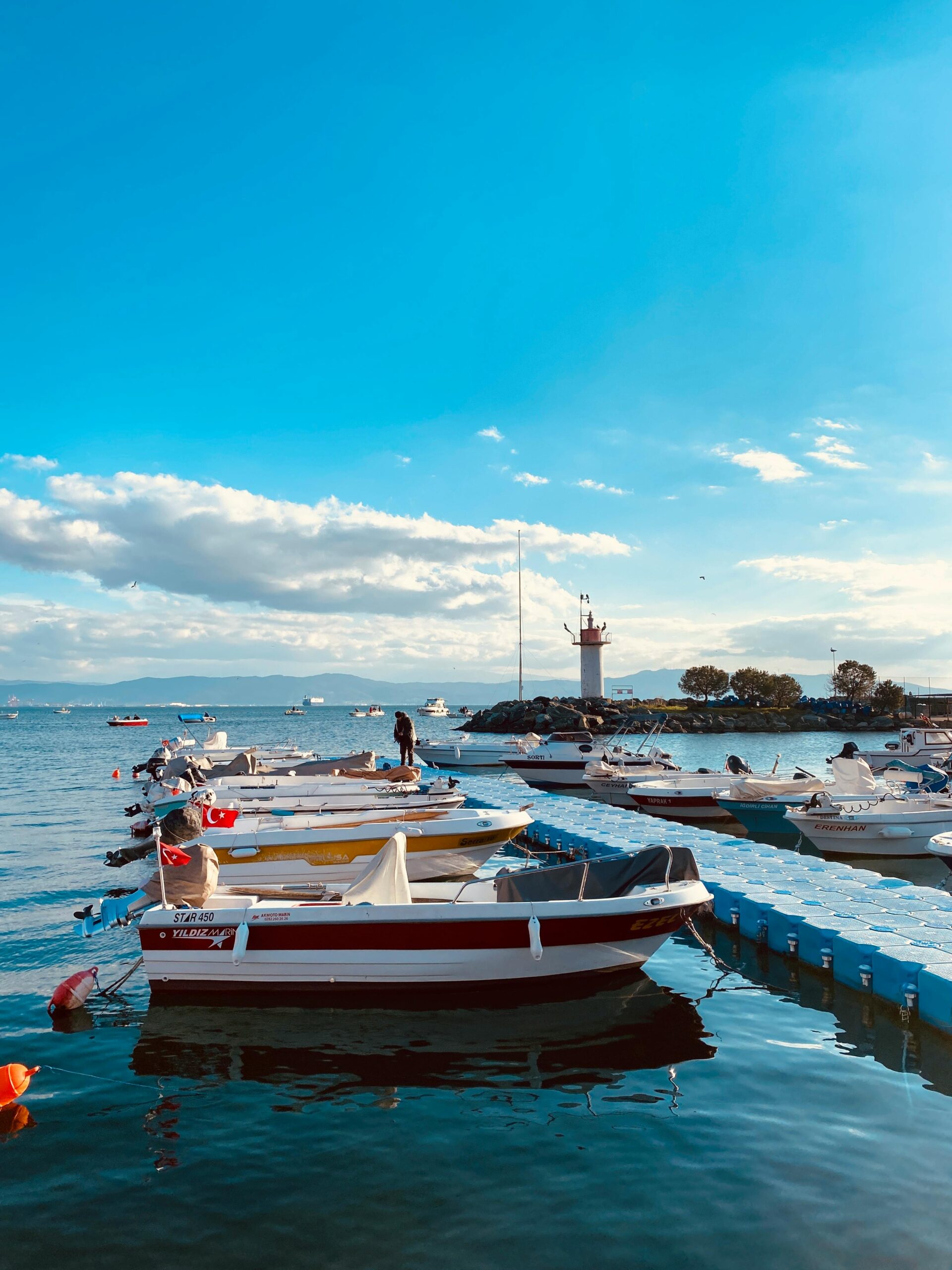 Scenic view of docked boats with a lighthouse under a blue sky in Yalova, Turkey.