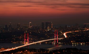 Stunning night view of the illuminated Bosphorus Bridge and Istanbul skyline under a red sky.