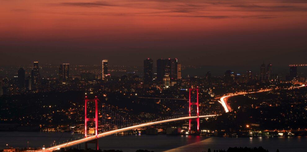 Stunning night view of the illuminated Bosphorus Bridge and Istanbul skyline under a red sky.